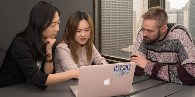 Three students looking at a laptop in an office meeting room.