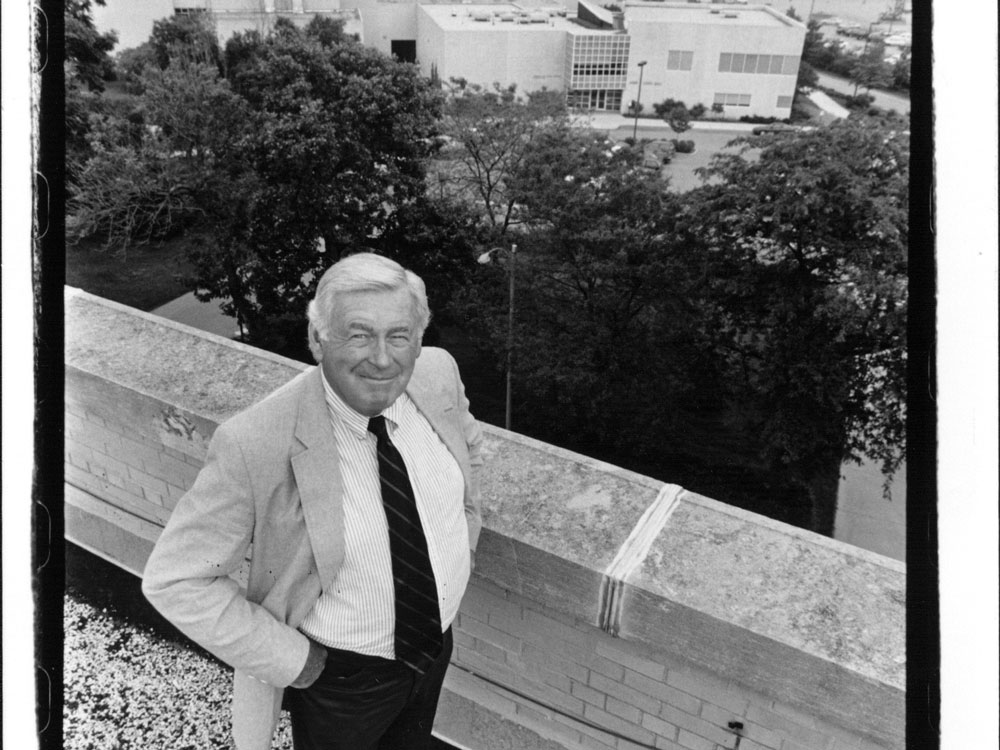 Bob Mulholland stands on top of a building in a black and white photo. You can see other buildings and a lake in the background.