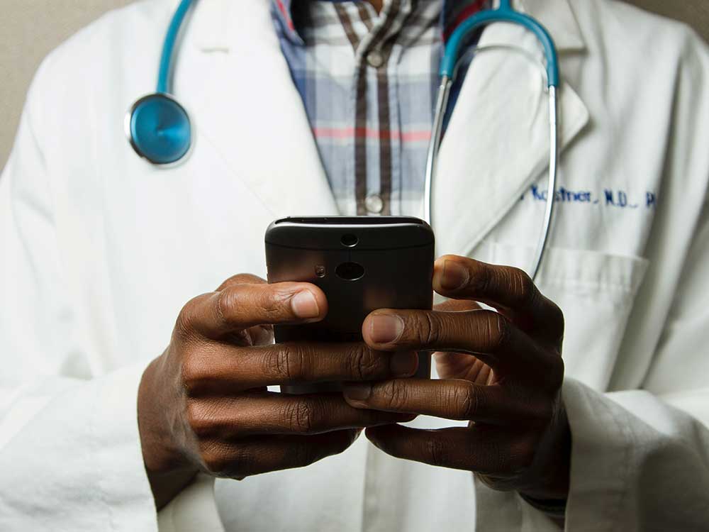 Photograph of a doctor in a white lab coat holding a cellphone.