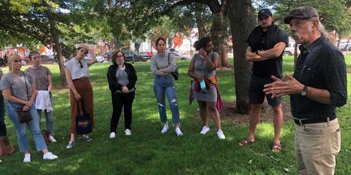 A group of students standing outside listening to a lecture.