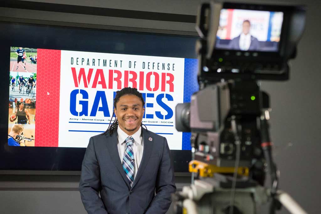 A video camera is pointed at a student as he records a "stand up" sports segment