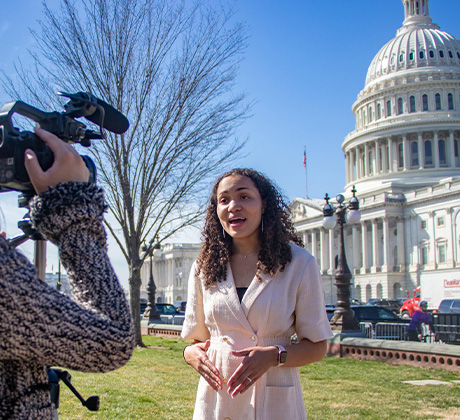 Student wearing a suit and carrying camera equipment in front of White House.