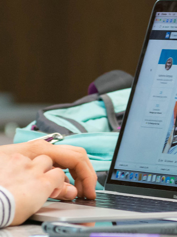 The hands of a student typing in LinkedIn on a laptop.