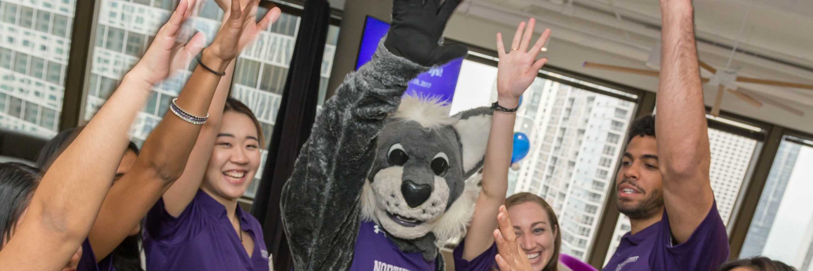 Students raise their hands in excitement with Willie the Wildcat