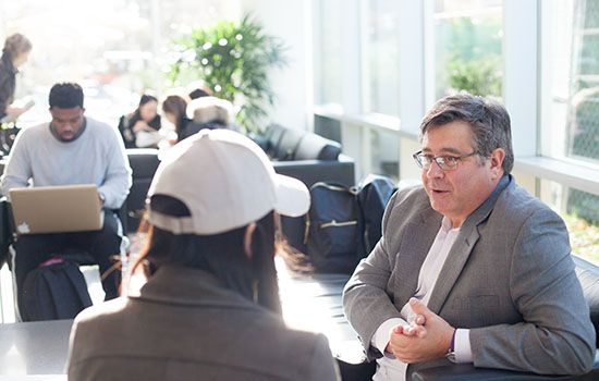 A faculty member talking to student, both seated.