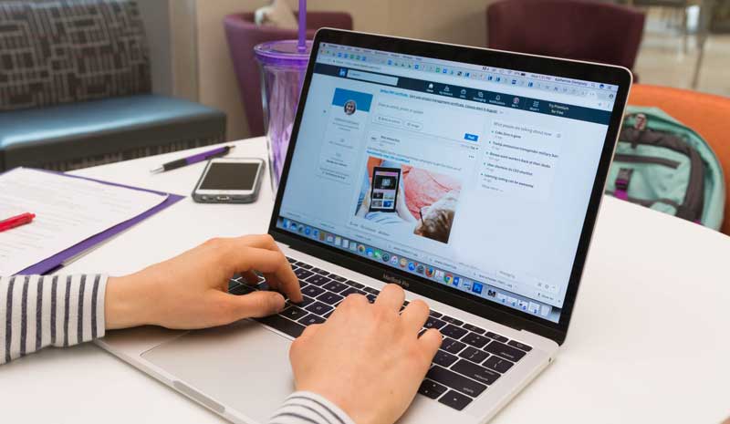 Hands typing on a laptop that has a LinkedIn page up on it with a purple Northwestern University cup on a table.