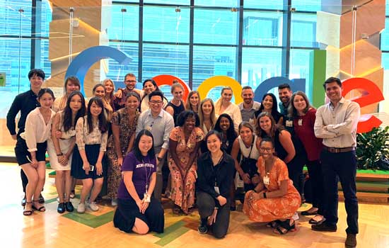 A large group of students pose for a photo in front of the Google sign at the Google office