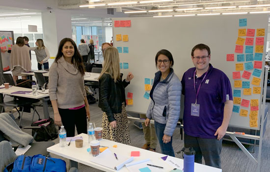 Students put sticky notes up on a white board in a modern-looking office space in San Francisco