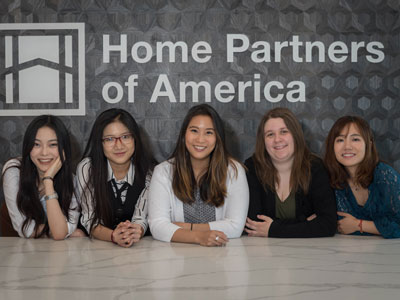 A team of five students pose for a photo by the Home Partners of America logo