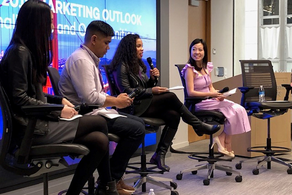 Four Medill IMC alumni sit in chairs at the front of a room and speak during a panel event