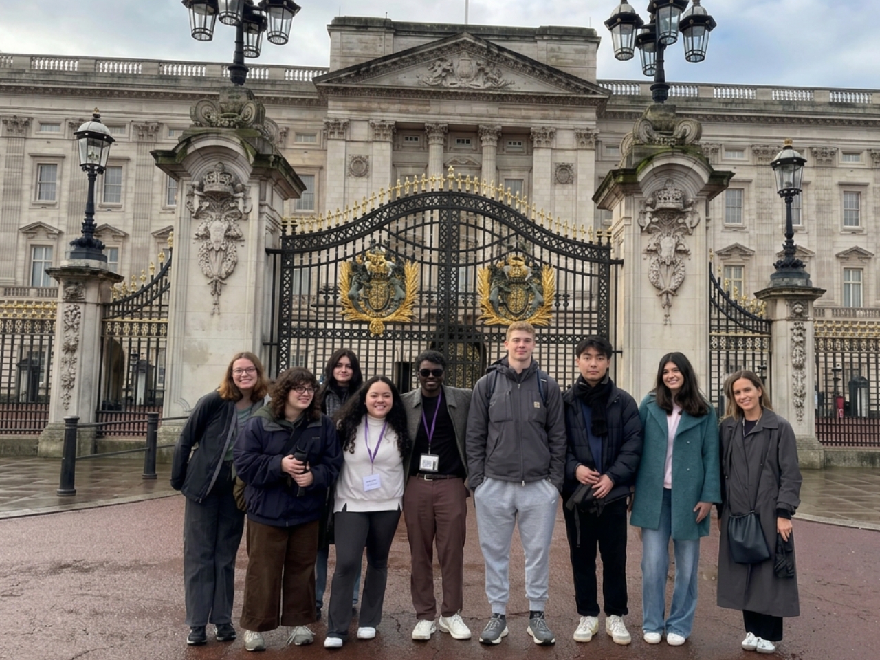 A diverse group of students poses smiling before Buckingham Palace’s ornate gates and grand façade on an overcast day.