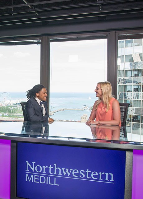 Two students speaking at the broadcast desk at Medill Chicago.