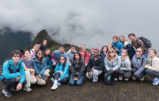 Diverse group of students and faculty smile on a mountain overlook, with misty green peaks behind them.