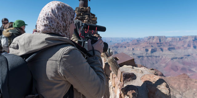 A woman looking through a camera at a canyon.