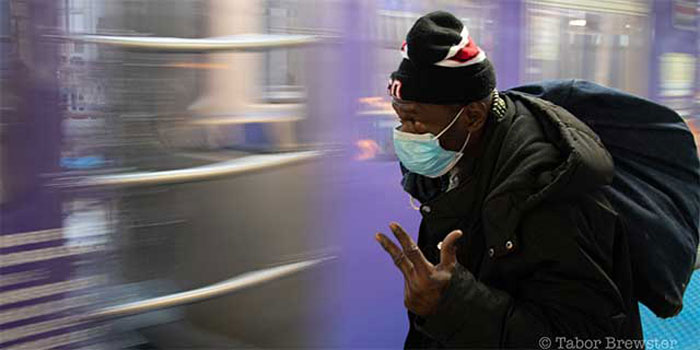 Mike Jones, wearing a medical mask, stands on a CTA platform, watching a train pass.
