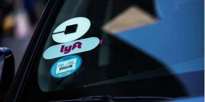 A car windshield displaying the logos for Uber and Lyft.