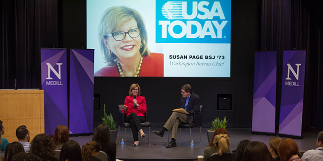 A woman speaks on stage to a classroom of students.