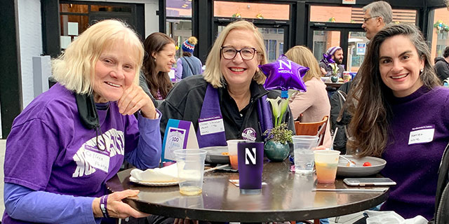 Medill alumni, dressed in purple, pose for a photo at a restaurant. 