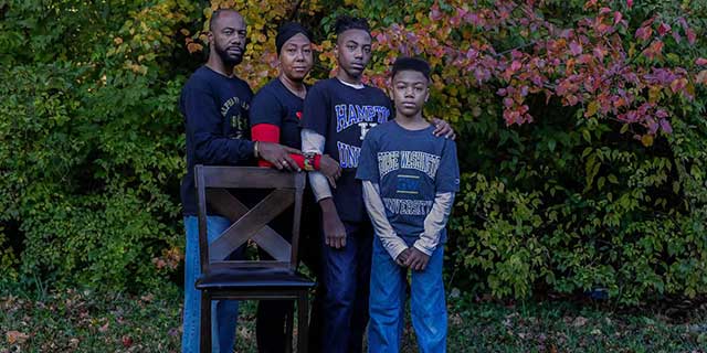 A family of four poses for a photo in front of an empty chair.