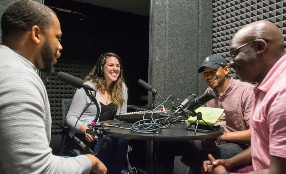 Four people seated around a table recording a podcast.