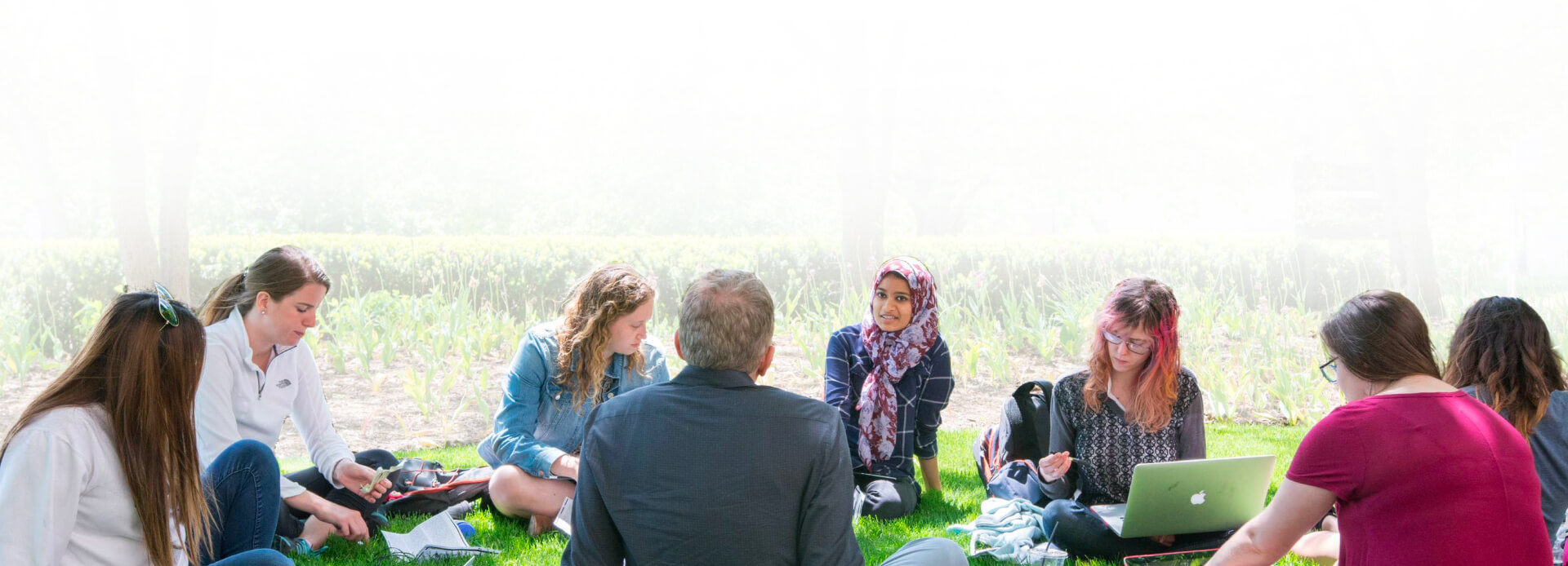 A class seated in a circle outside in the grass.