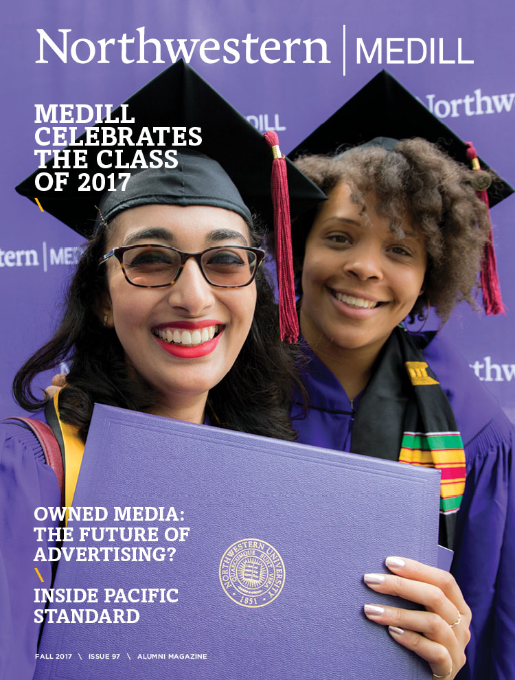 Two Medill students pose for a photo wearing a cap and gown at graduation and holding their diploma