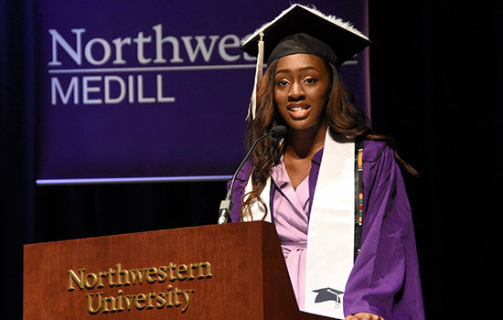 A student stands at a lectern while wearing a cap and gown
