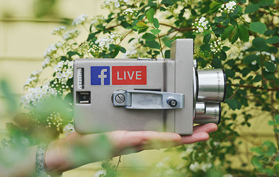A person holds a video camera with the Facebook Live logo on the side of it.