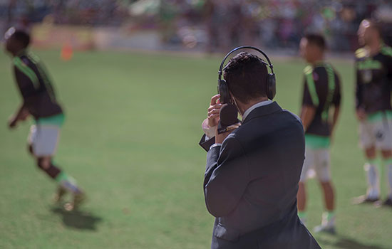 Sports commentator watches soccer game from the sidelines
