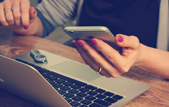 A person holds a cell phone while also working on a laptop computer.