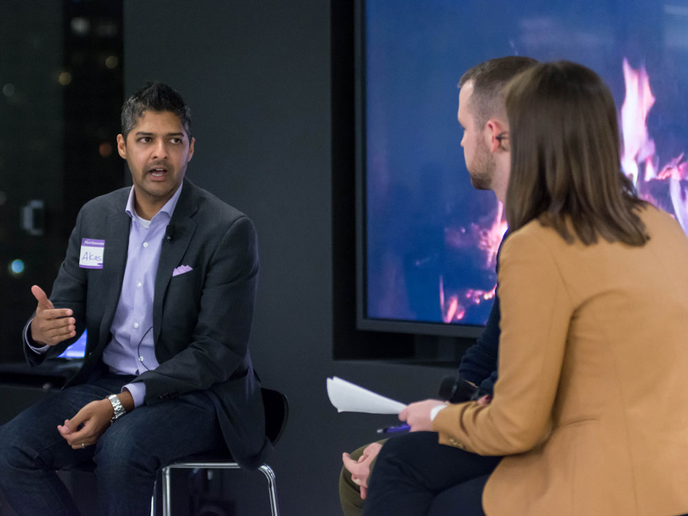 A man talks on stage with two students