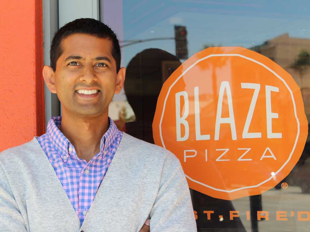 A man stands in front of a glass window with the Blaze Pizza logo on it