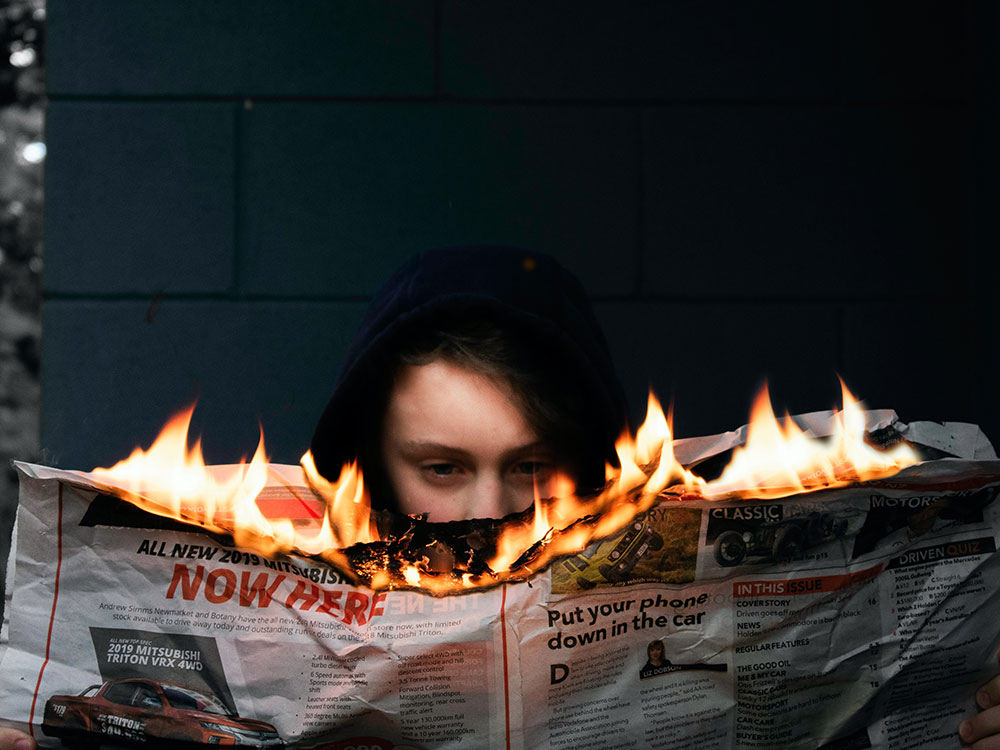 Photograph of a person reading a newspaper that is on fire.