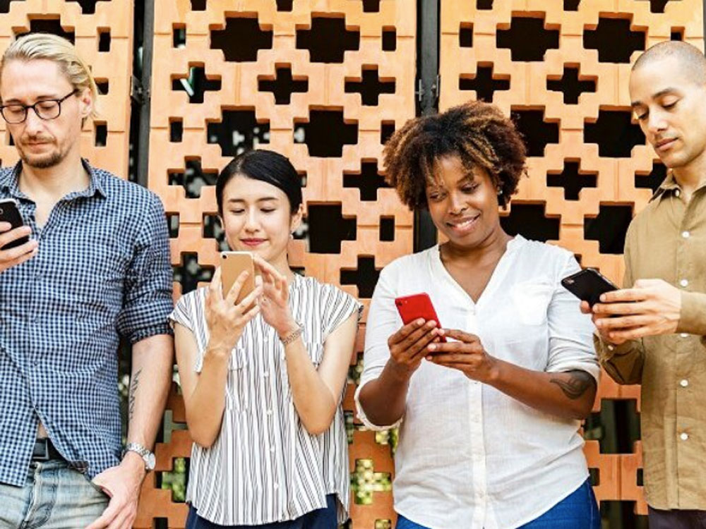 Four people are standing up and looking at their cell phones in their hands