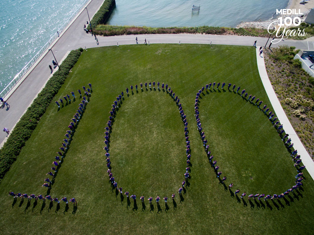 A large group of students wearing purple shirts form the number "100."