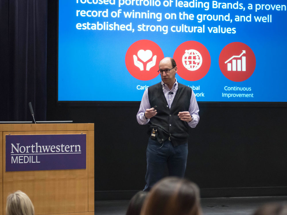 Colgate COO Justin Skala stands on stage and speaks to IMC students