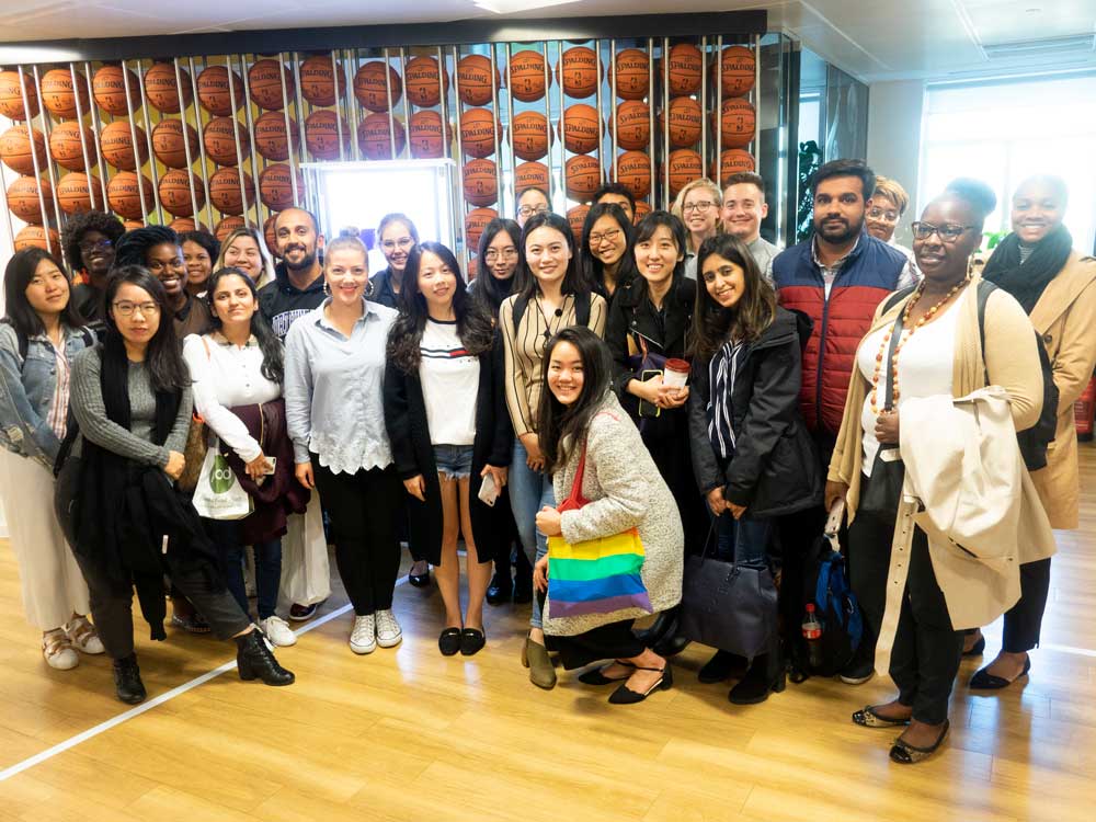 A group of students pose for a photo with basketballs in the background on the wall