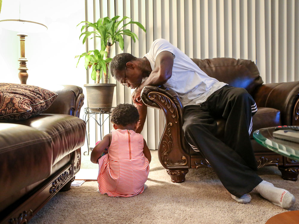 A man sits on a chair by a young girl who sits on the floor