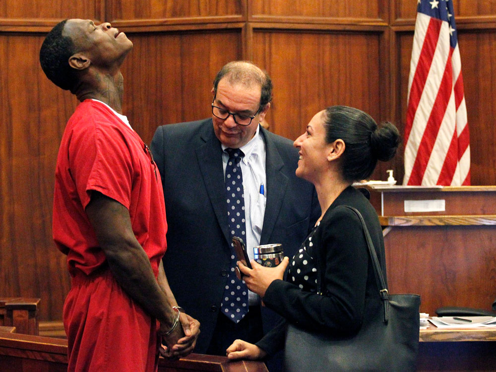 A man in a prison suit in handcuffs drops is head back in relief while his lawyers stand nearby