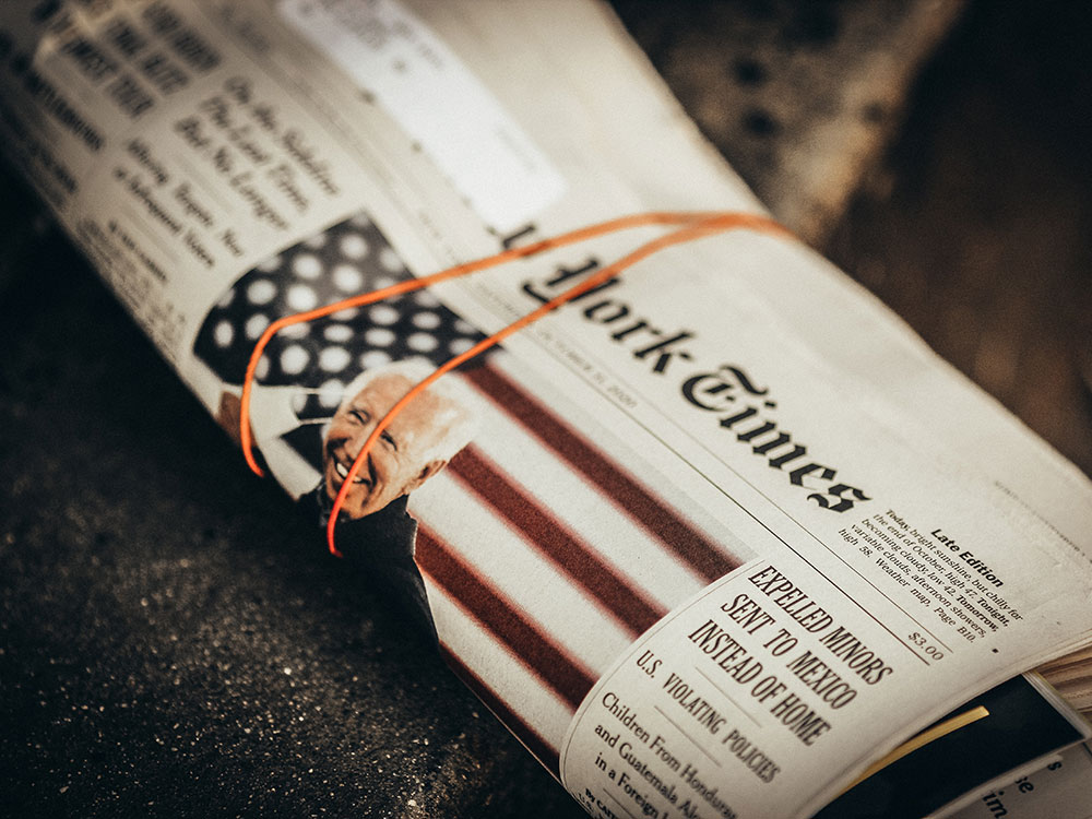 A rolled up issue of the New York Times displays an image of Joe Biden in front of an American flag backdrop.