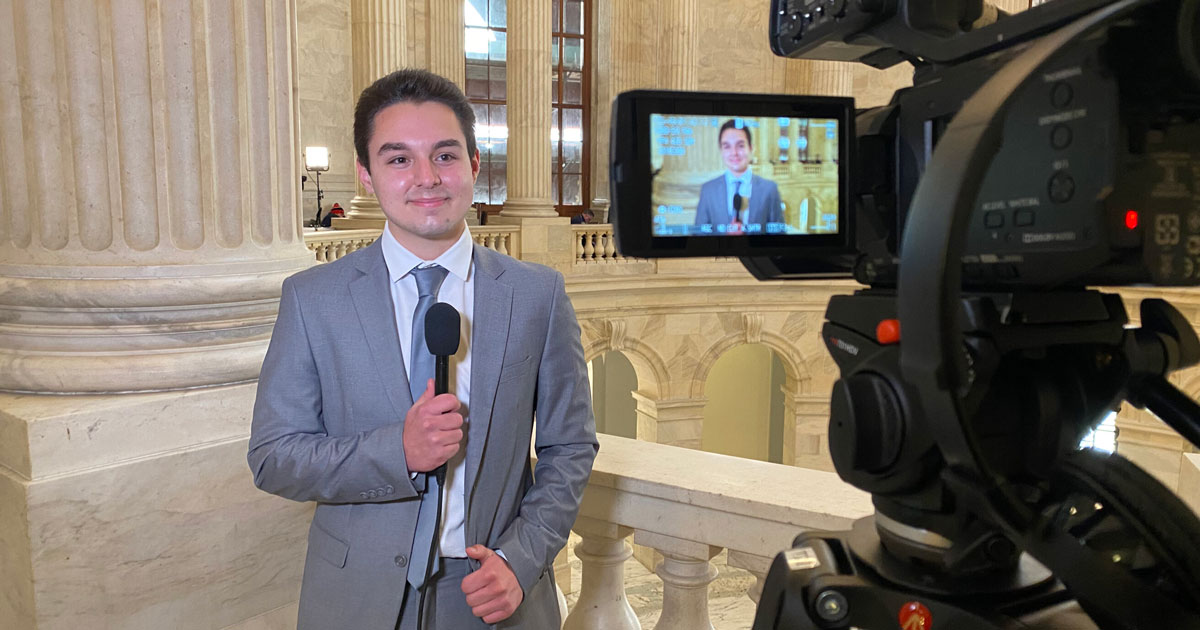 A student in a suit doing a news report inside the Capitol.