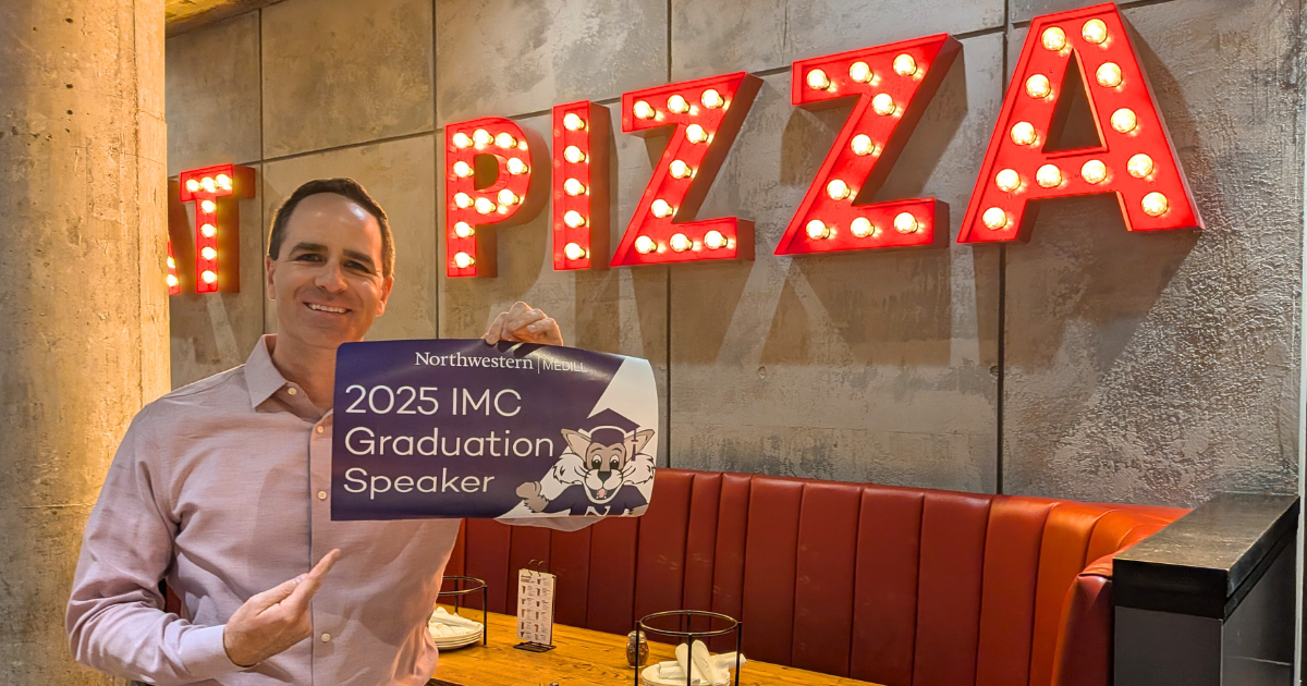 A man holding a sign that says 2025 IMC Graduation Speaker.