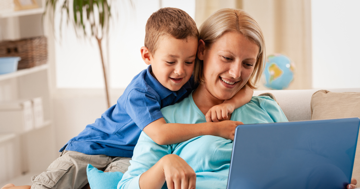 A mother and a son sit on the couch looking at a laptop screen.