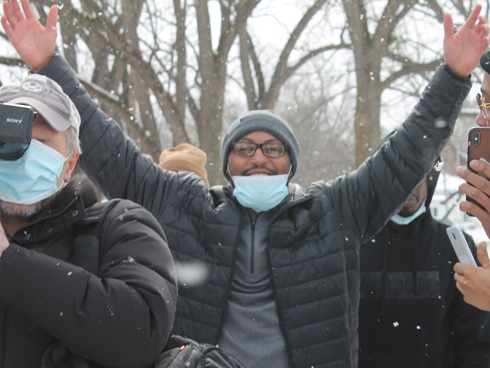 Kenneth Nixon stands outside in the snow, raising his arms triumphantly. 