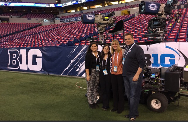 IMC Certificate students on the sidelines at a football stadium next to a large camera rig.