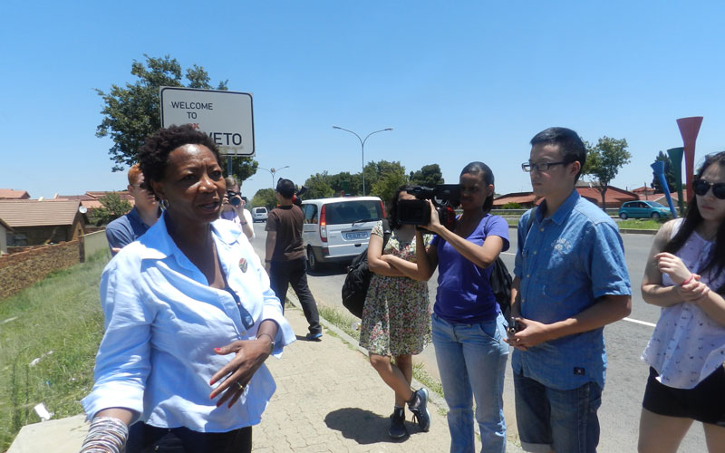 A woman in a blue button down shirt speaking to a group of students.